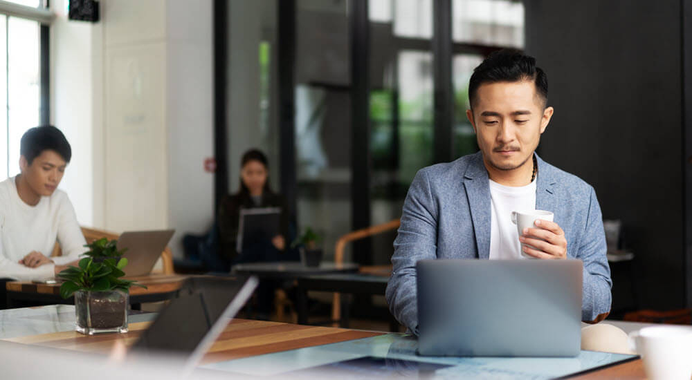 young man sitting at laptop drinking a coffee